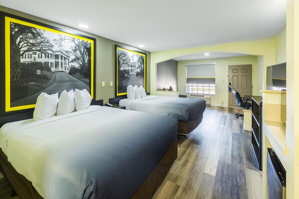 A hotel room with two beds, a desk, a chair, a TV, and large framed pictures on the walls.