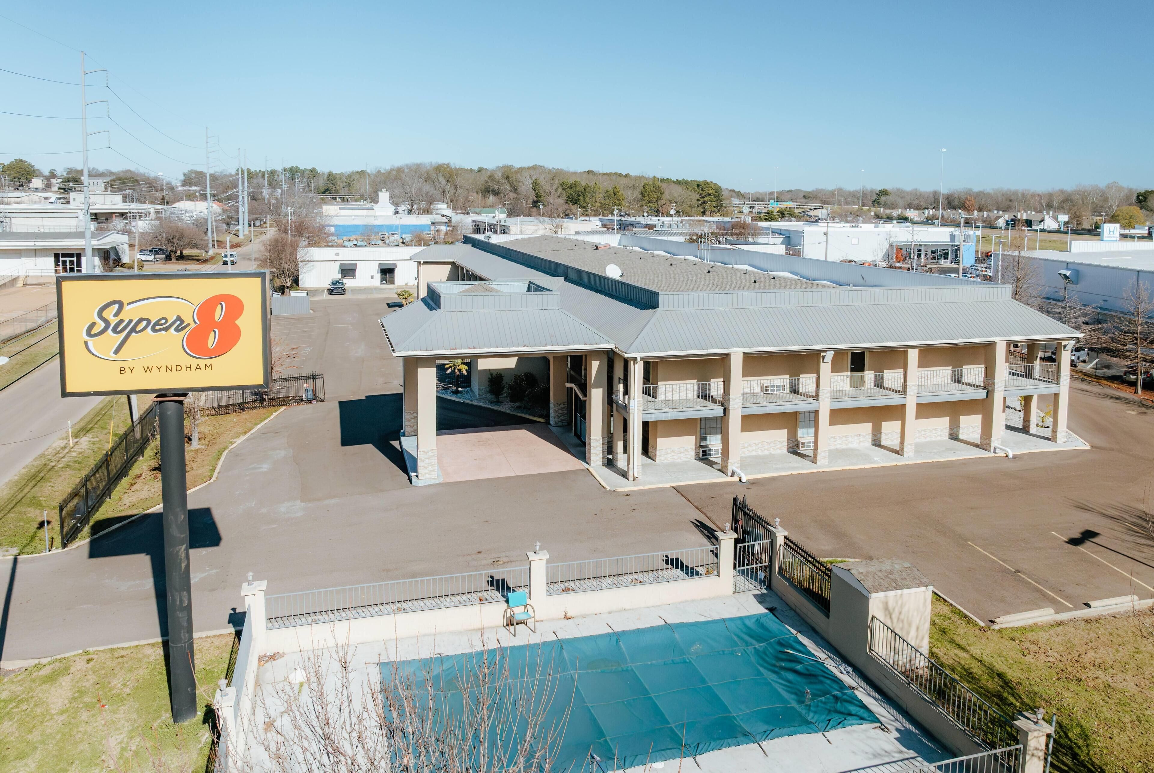 A multi-story building with a large sign reading "Super 8 by Wyndham" and a swimming pool in front.