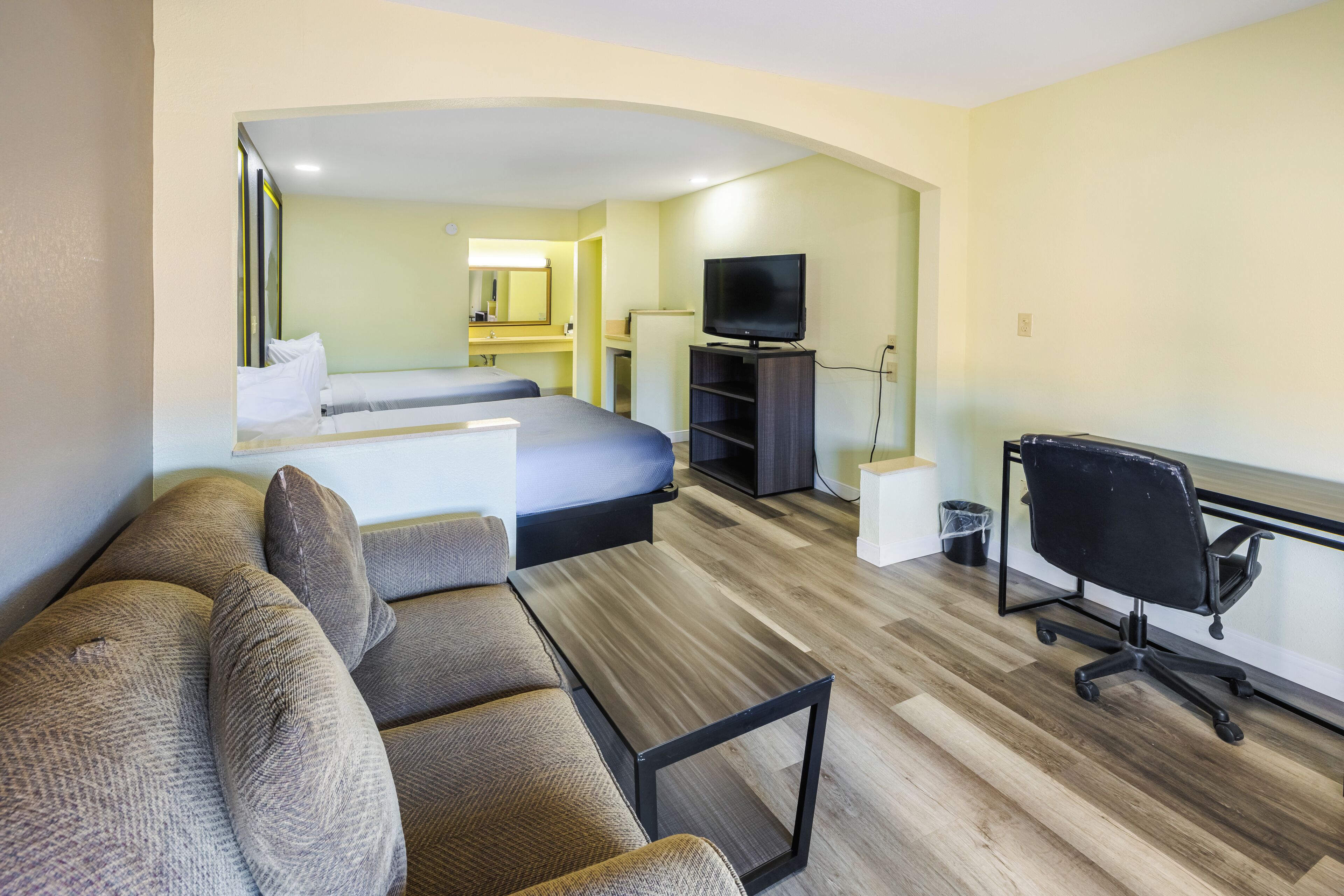 A hotel room with a sofa, a bed, a desk, a chair, and a television.