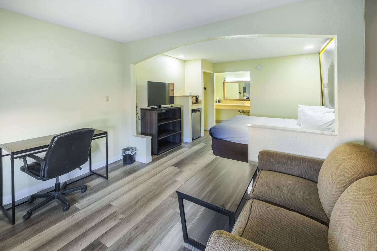 A hotel room with a desk, office chair, bed, and a small kitchenette.
