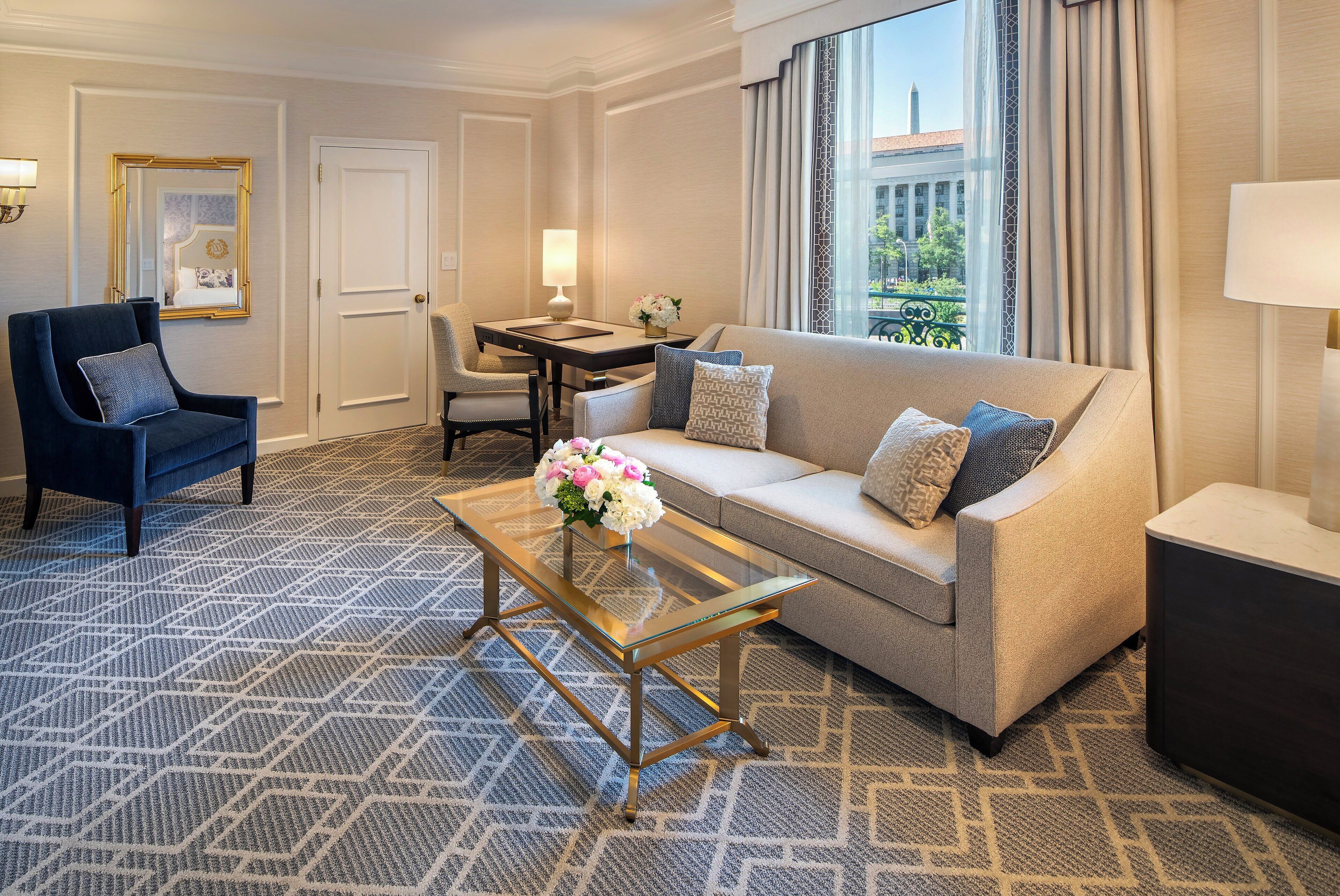 Quarto de hotel com sofá, poltrona e uma pequena mesa com um vaso de flores.