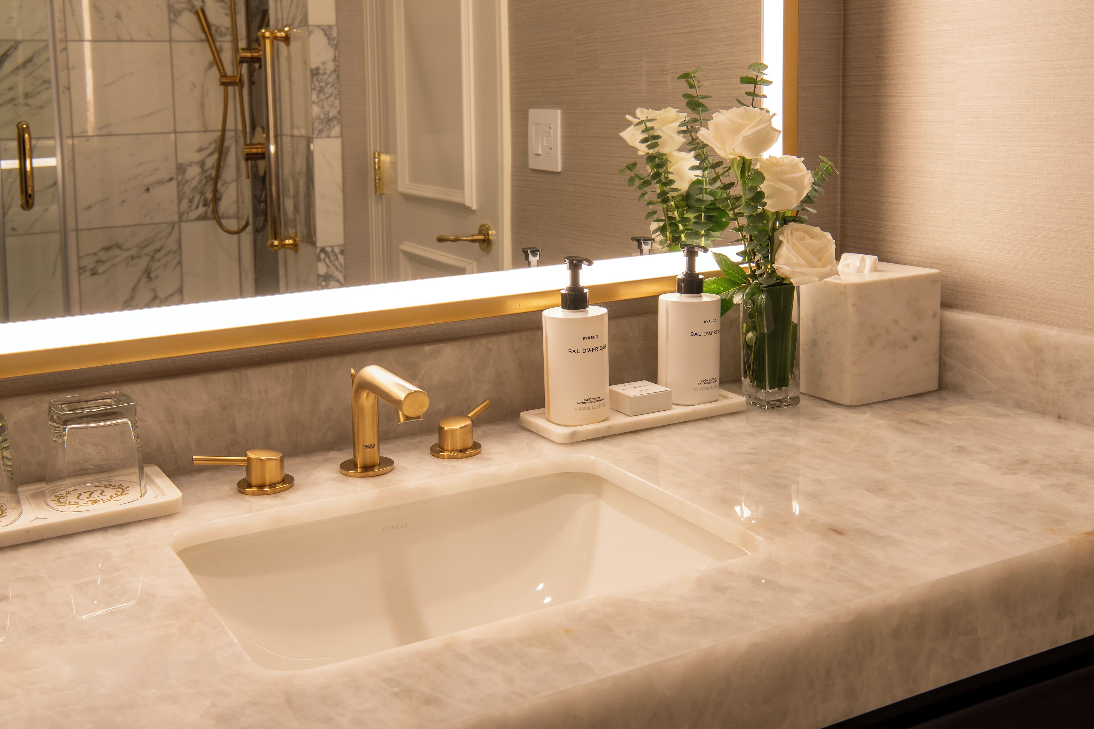Un bagno con uno specchio grande, un lavabo con accessori dorati e articoli da bagno sul ripiano.