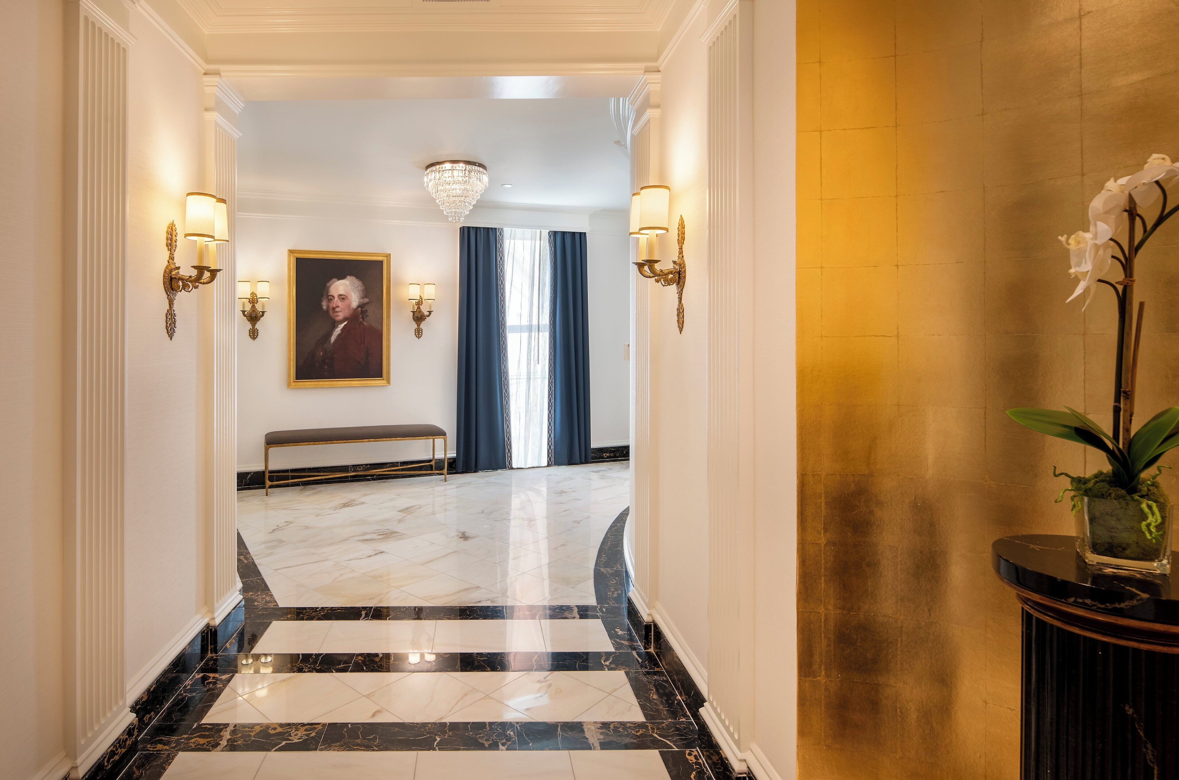 A hallway with marble flooring, a bench, wall sconces, a chandelier, and a framed portrait.