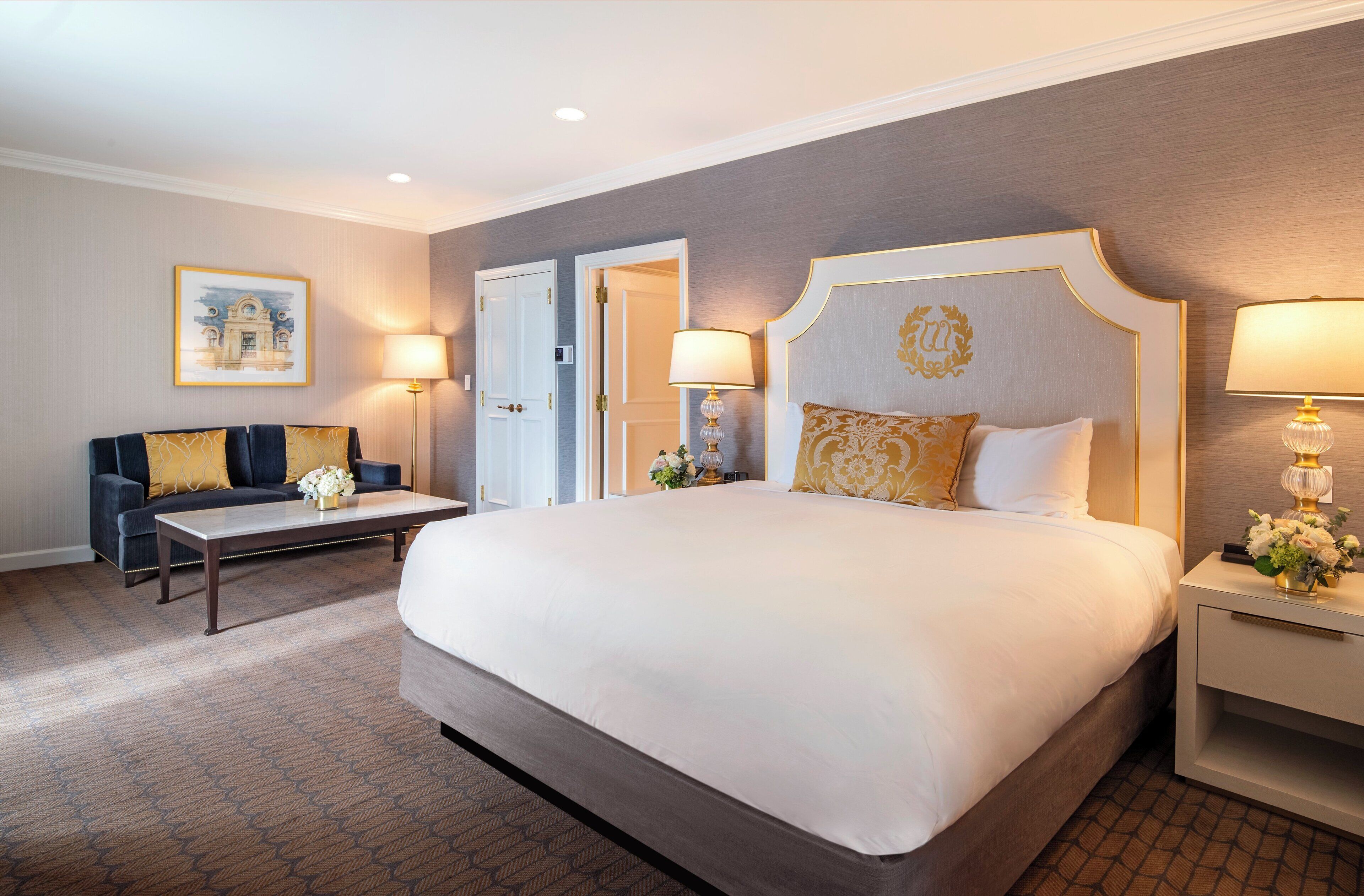 A hotel room with a large bed, a sofa, two bedside tables with lamps, and a framed picture on the wall.