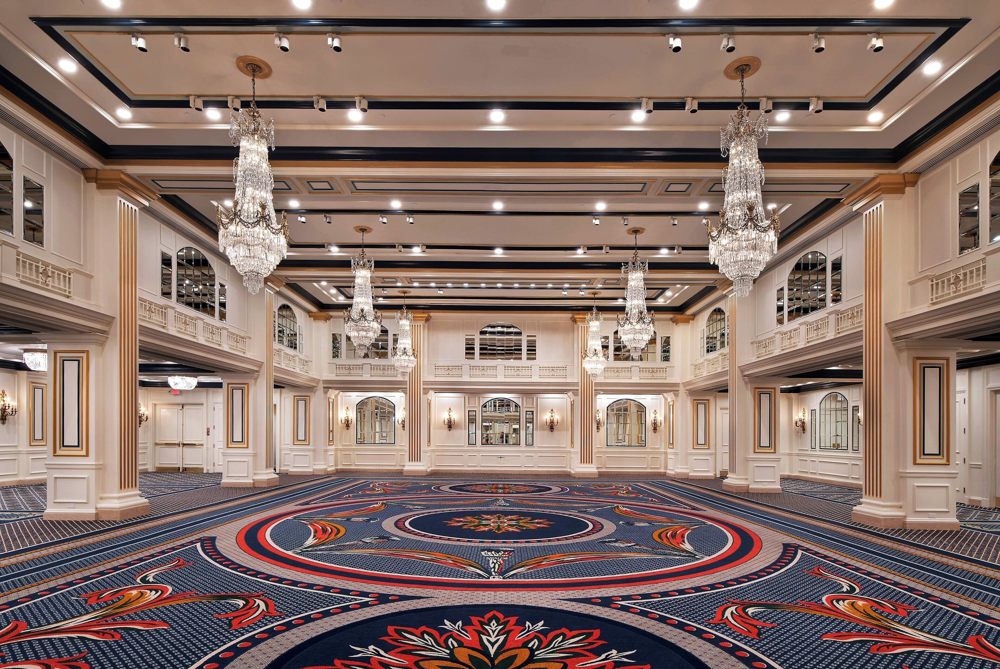 A grand hotel lobby with a large, ornate chandelier, high ceilings, and a patterned carpet.