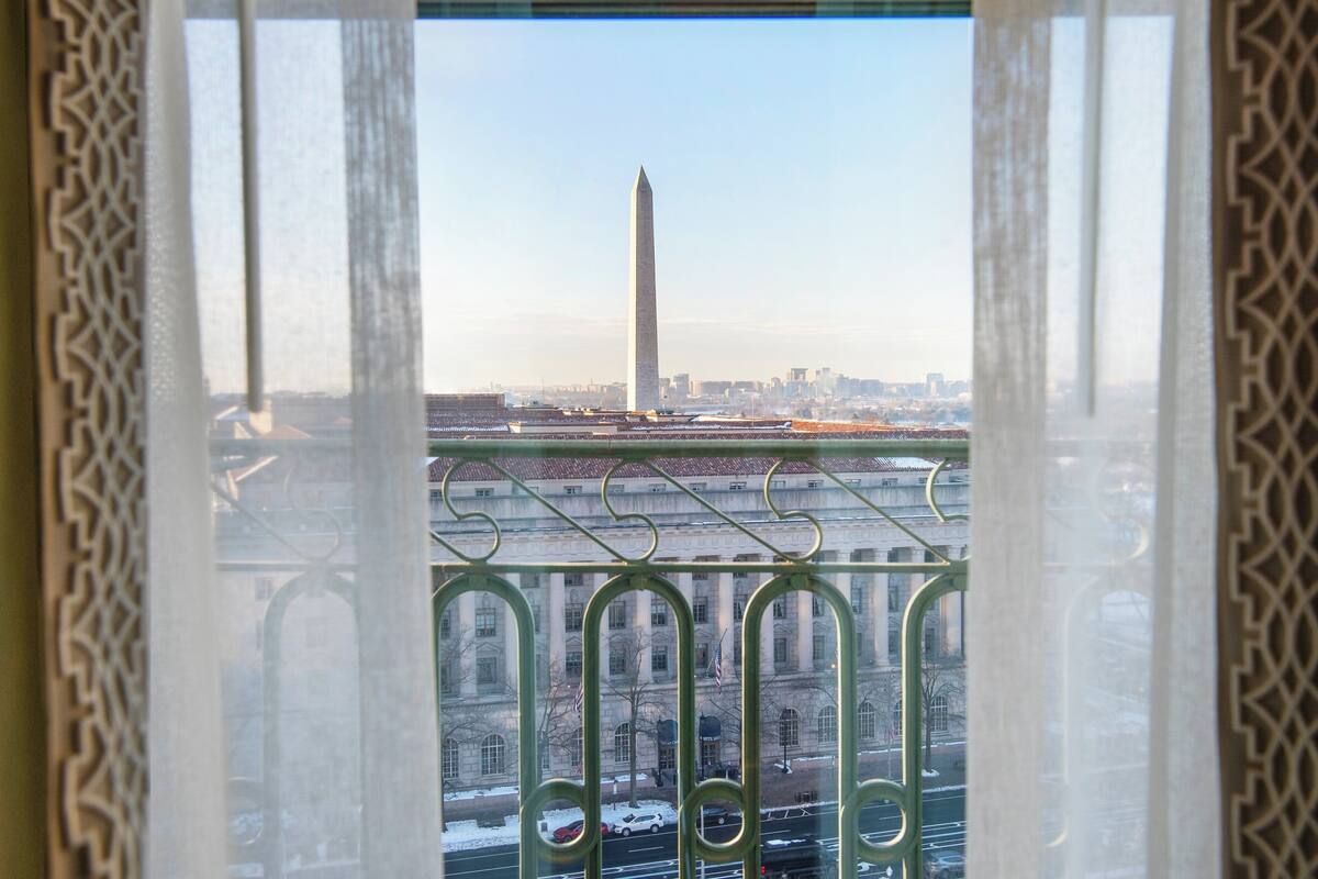 A view of the Washington Monument through a window with ornate metal railings.