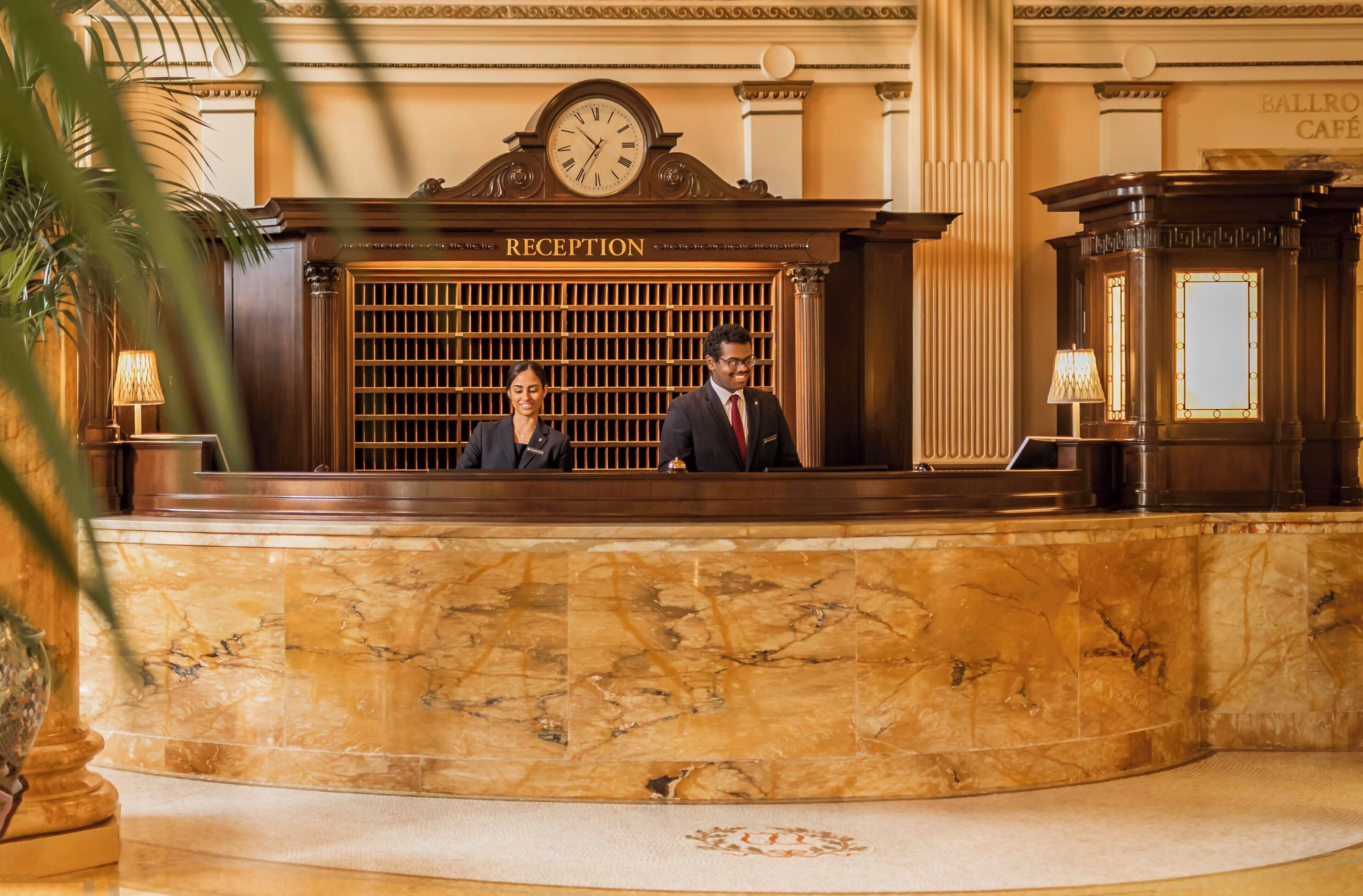 A reception desk with a clock above it, a marble floor, and a columned wall.