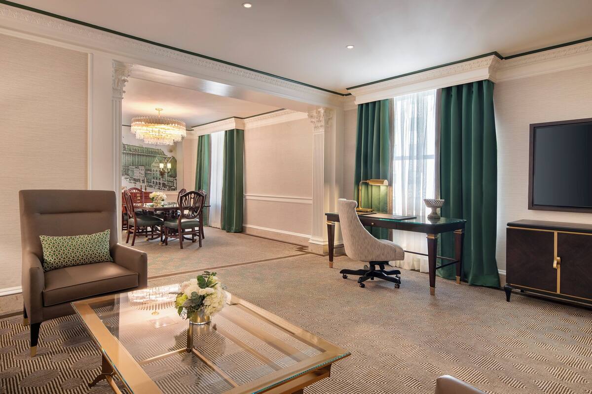 A hotel room with a dining area, a TV, and a desk with a lamp.