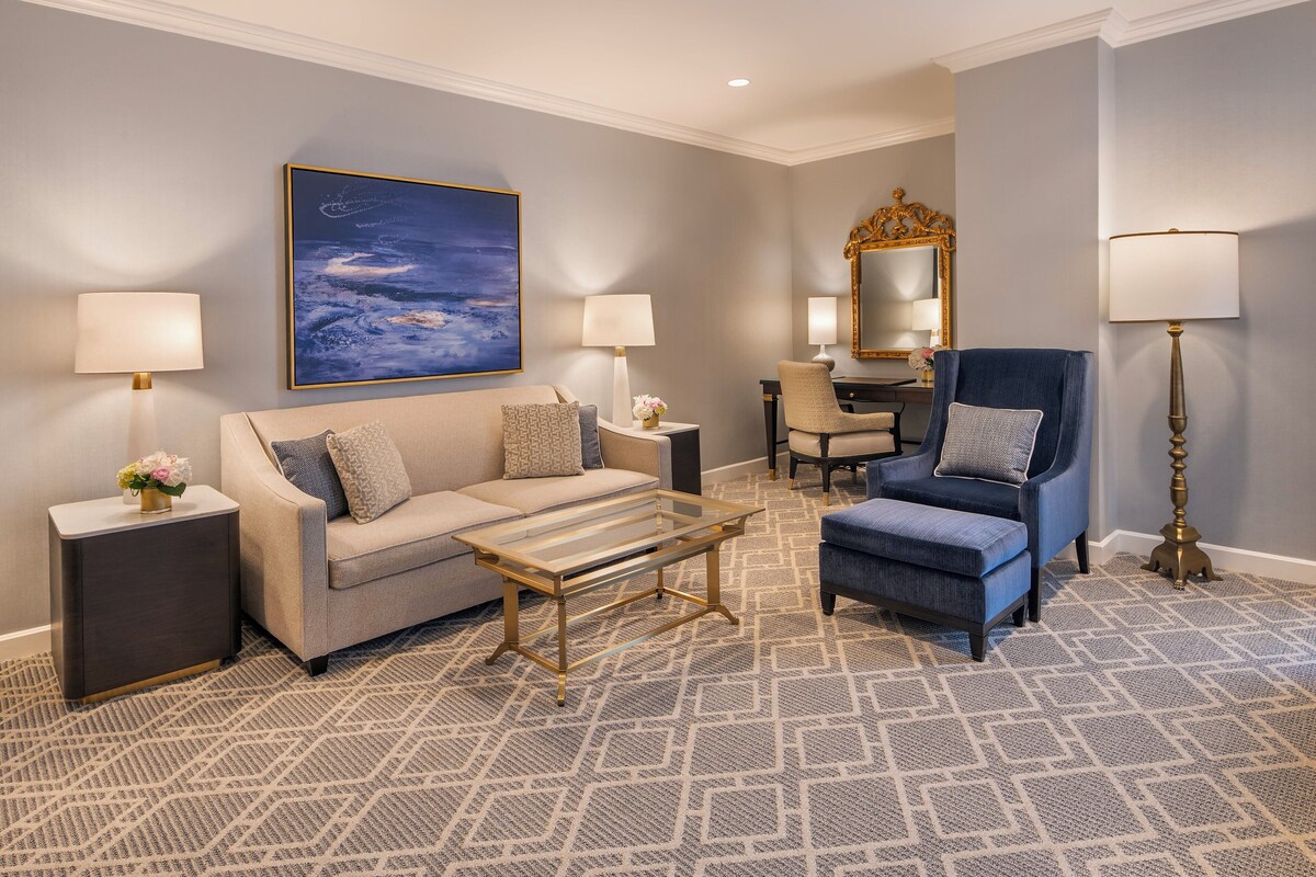 A modern living room with a sofa, armchair, and coffee table, a large painting, and a mirror.