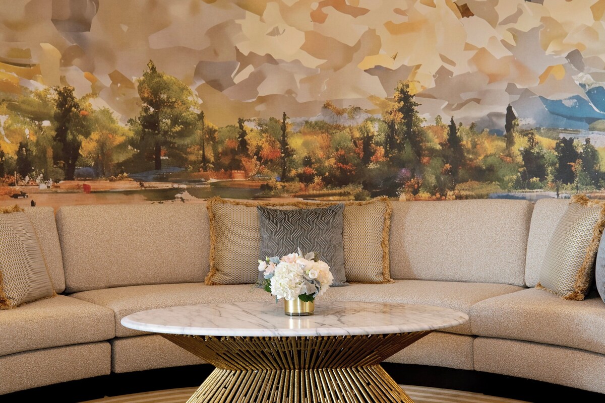 A modern living room with a curved sofa, a marble coffee table, and a decorative wall mural.