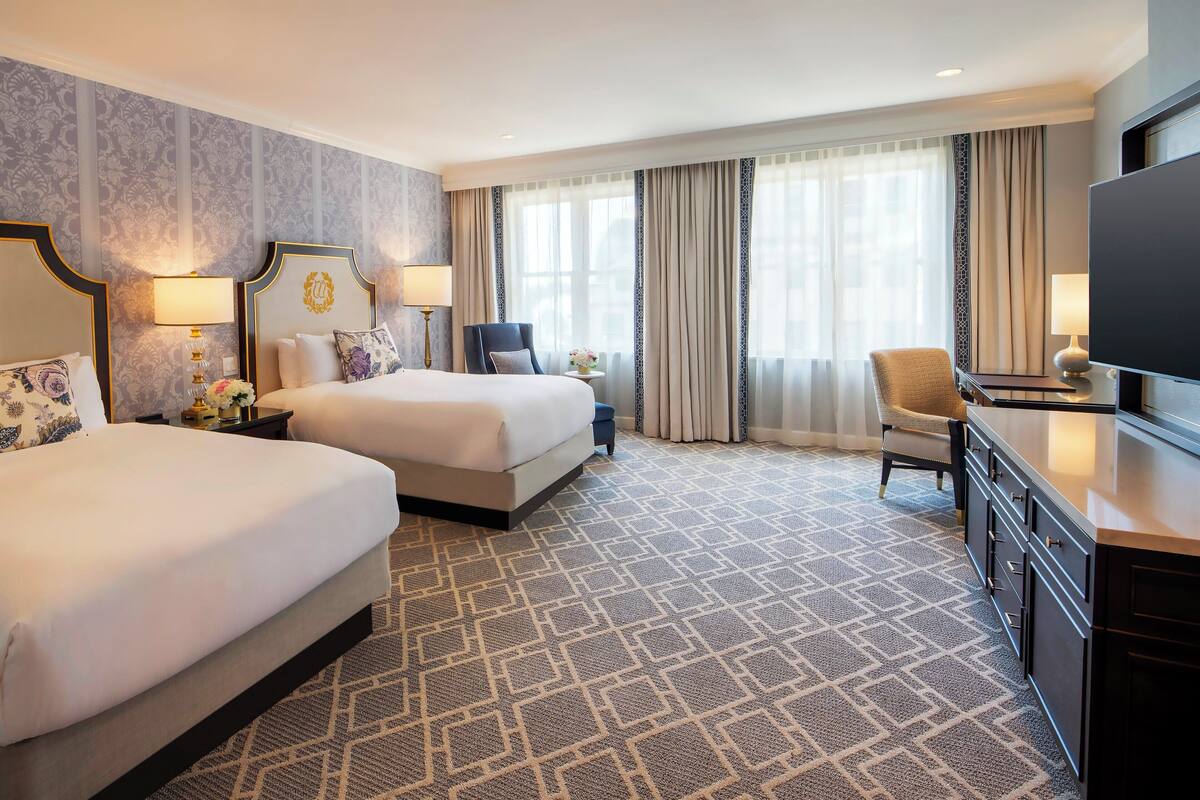 A hotel room with two beds, a TV, a desk, and a chair.