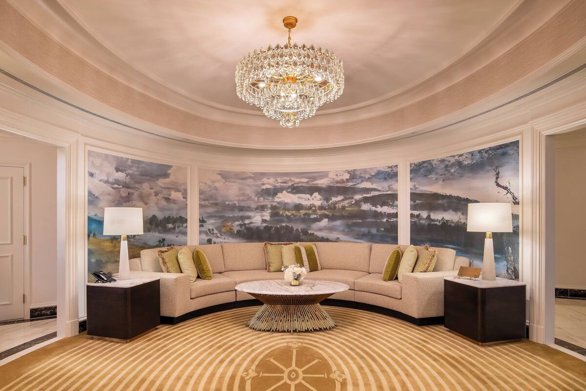 A luxurious living room with a curved sofa, a central coffee table, and a large landscape painting on the wall.