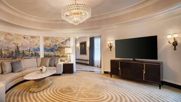 A luxurious living room with a large chandelier, a flat-screen TV, a sofa with decorative pillows, a coffee table, and a patterned carpet.