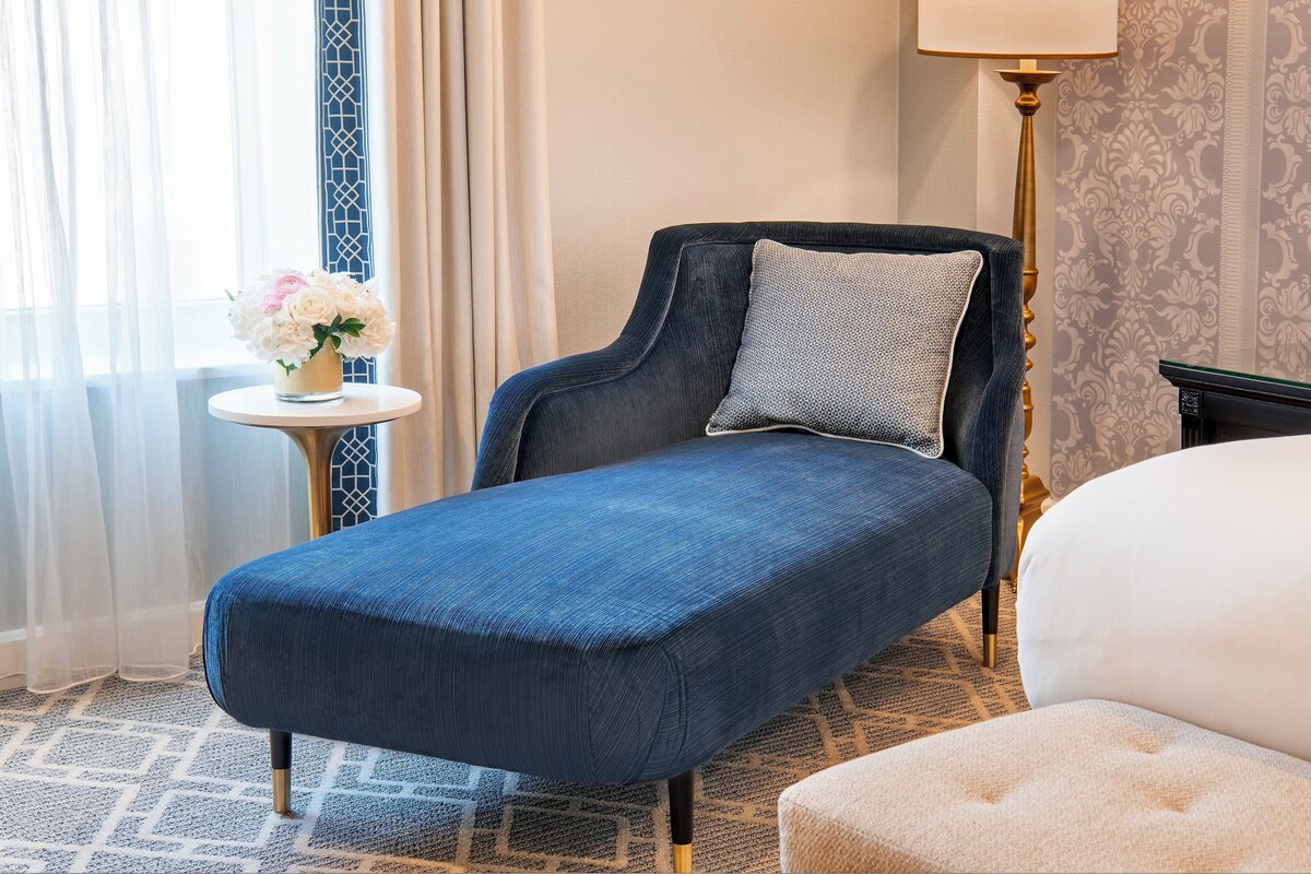 A single bed with a white headboard, a small round table with a vase of flowers, and a floor lamp.