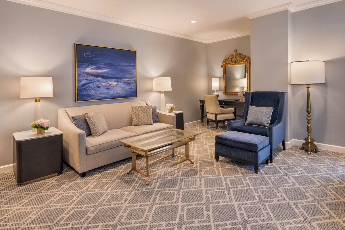A modern living room with a sofa, armchair, and coffee table, a large painting, and a mirror.