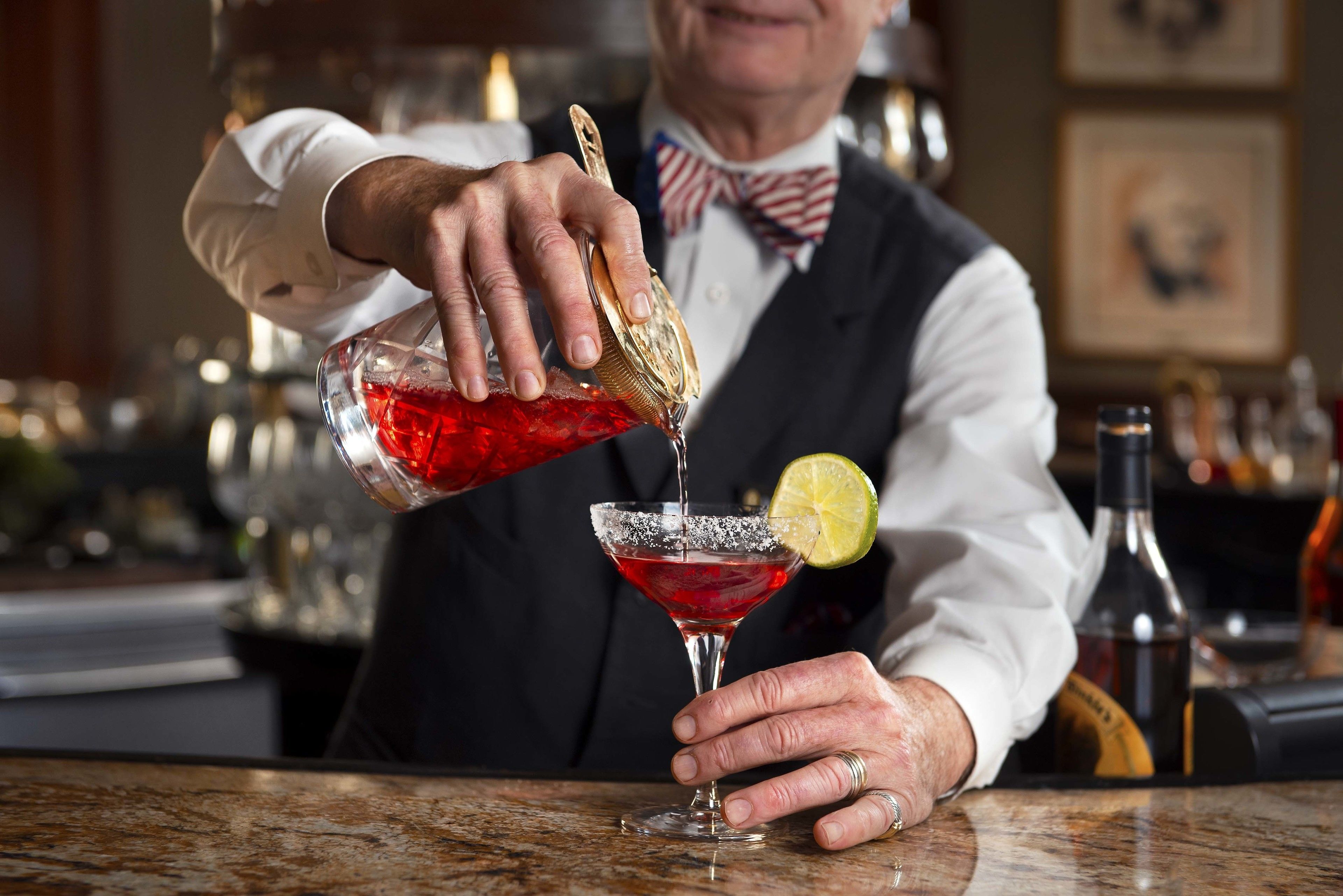 Un barman verse une boisson dans un verre à martini, qu’il garnit d’une tranche de citron vert.