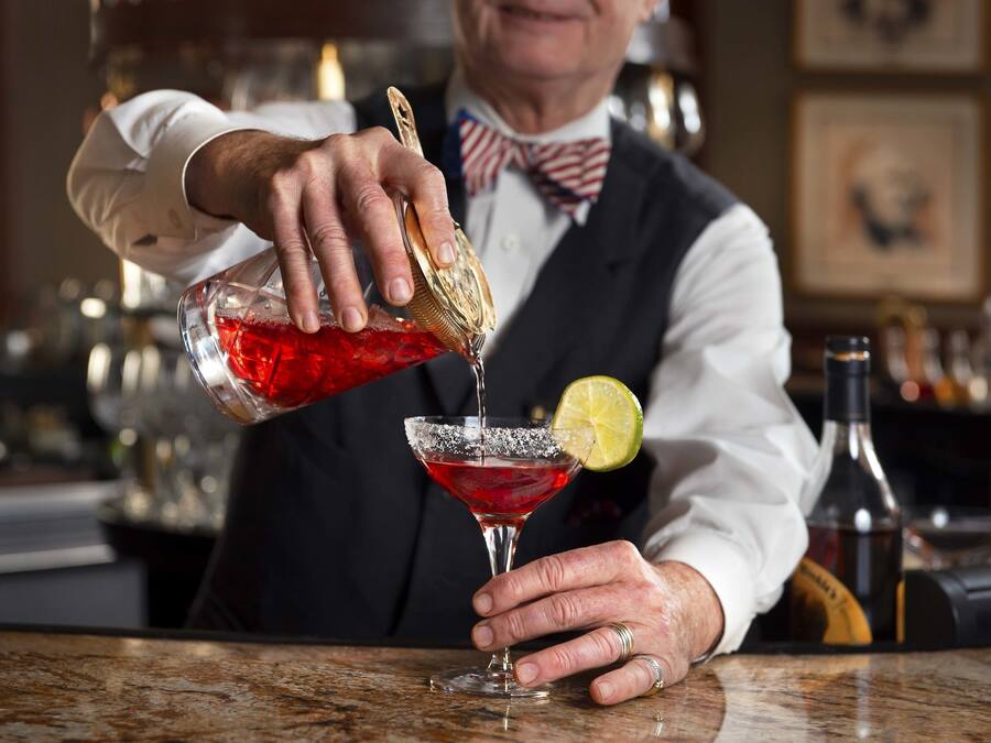 A bartender pouring a drink into a martini glass with a lime garnish.