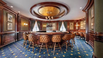 Un elegante bar con una mesa redonda, varios taburetes y retratos enmarcados en las paredes.
