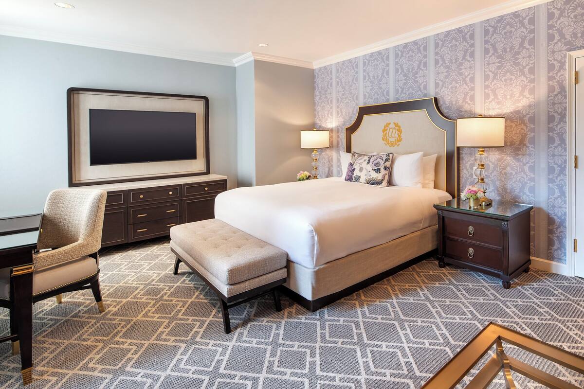 A hotel room with a large bed, a desk, a chair, and a TV.