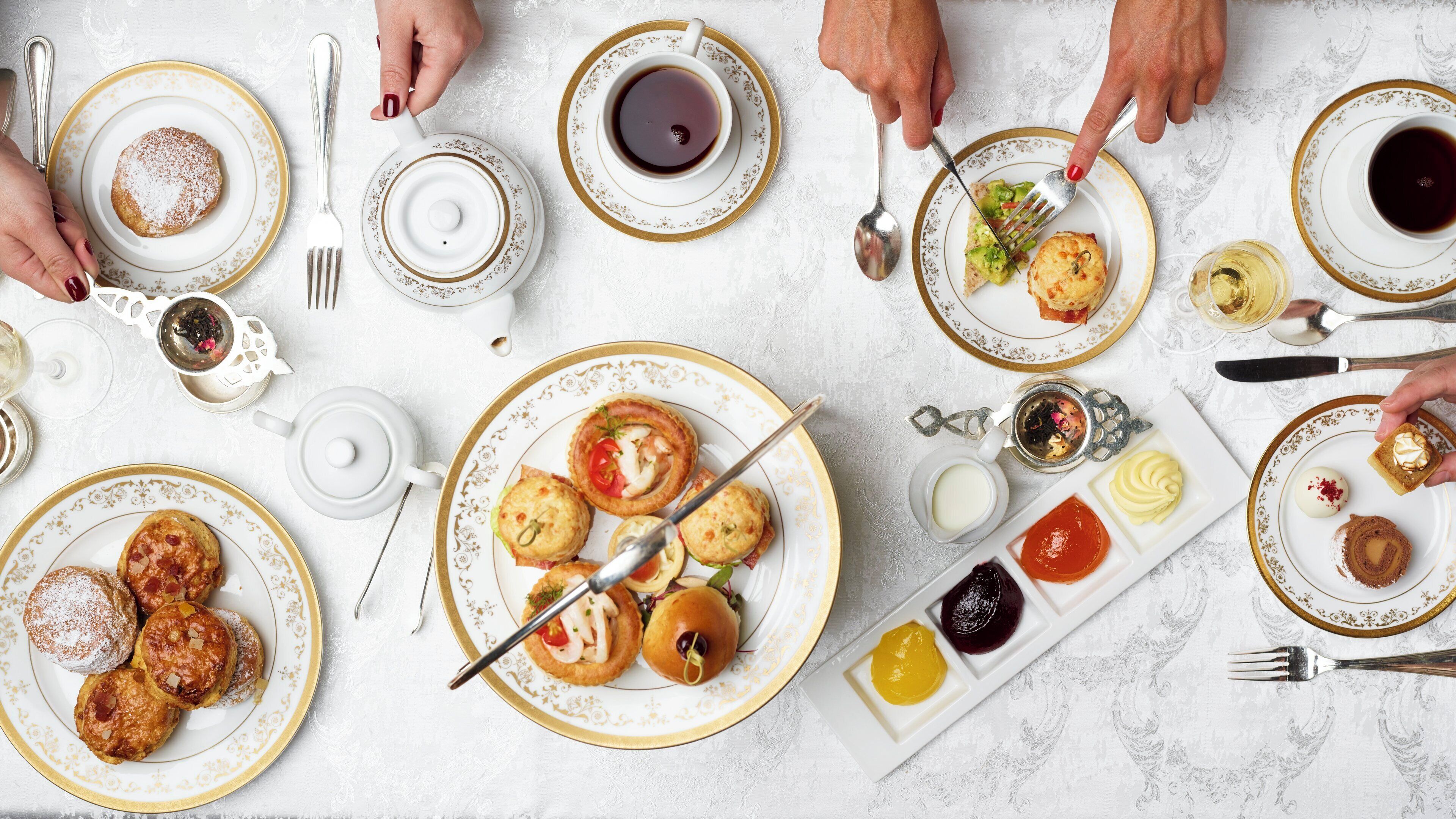 A table set with various pastries, a teapot, and multiple cups of tea.