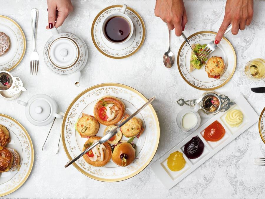 A table set with various pastries, a teapot, and multiple cups of tea.