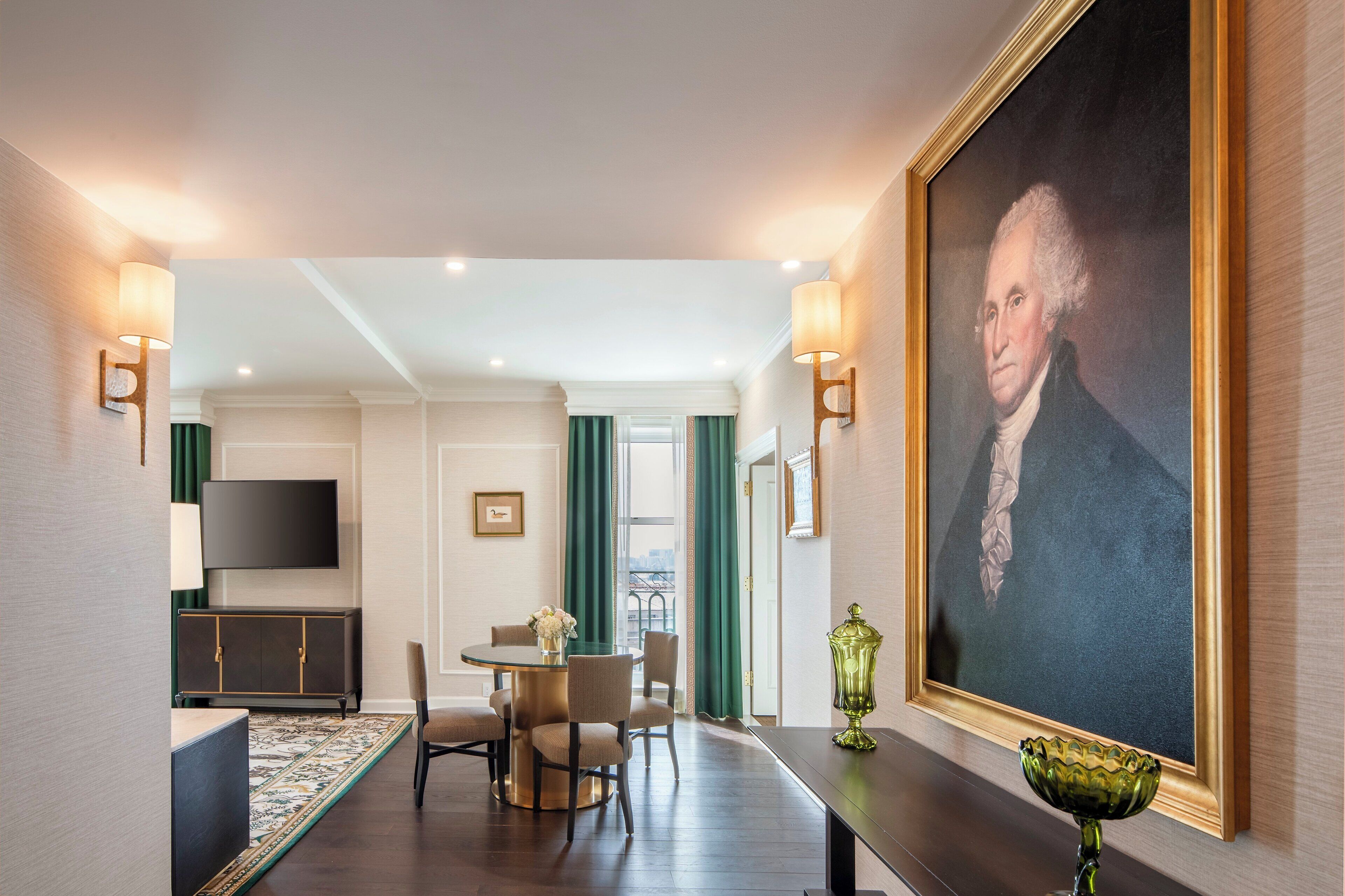 A hotel room with a dining area, a large portrait on the wall, and a TV mounted on the wall.