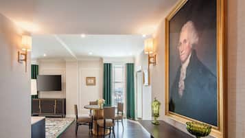A hotel room with a dining area, a large portrait on the wall, and a TV mounted on the wall.