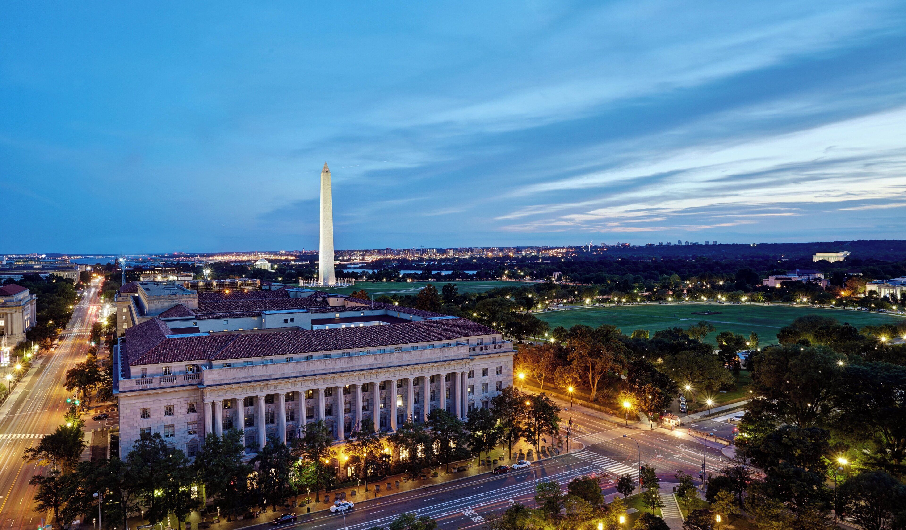 A large building with a prominent central column, surrounded by a well-lit urban area with roads and greenery.