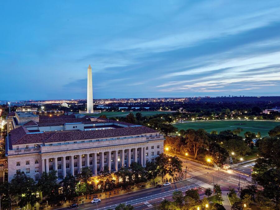 A large building with a prominent central column, surrounded by a well-lit urban area with roads and greenery.
