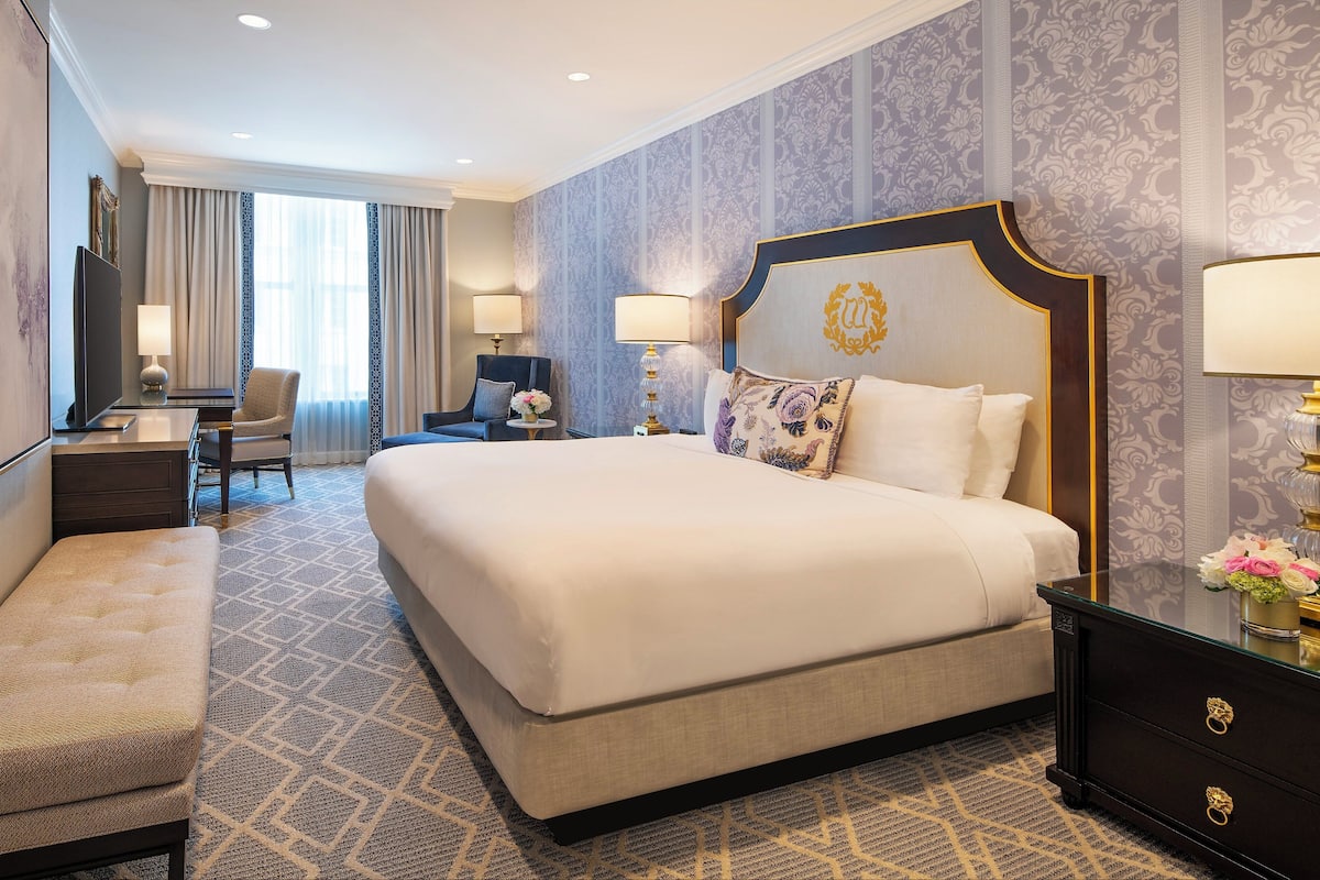 A hotel room with a large bed, a desk with a chair, a sofa, and a TV.