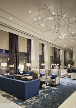 A modern restaurant with a central bar area, seating arrangements, and large windows offering a view of greenery. at Hotel Nikko San Francisco