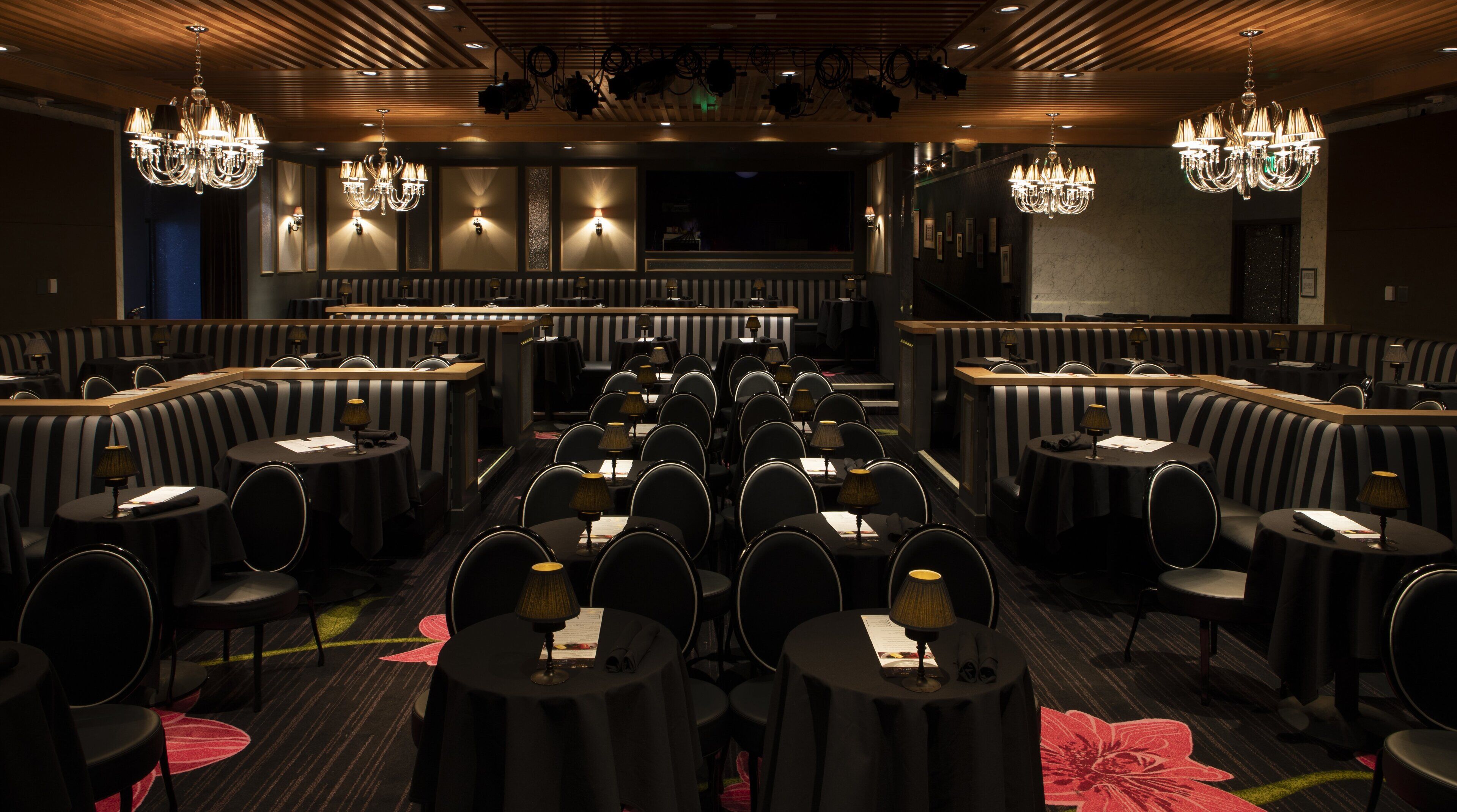 Un restaurant avec des banquettes à rayures noires et blanches, des tables rondes avec des lampes et des lustres.