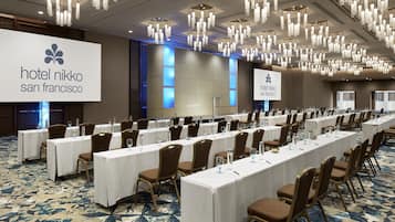 Un salón de conferencias en el Hotel Nikko San Francisco, con largas mesas, sillas y una pantalla grande que muestra el nombre del hotel.