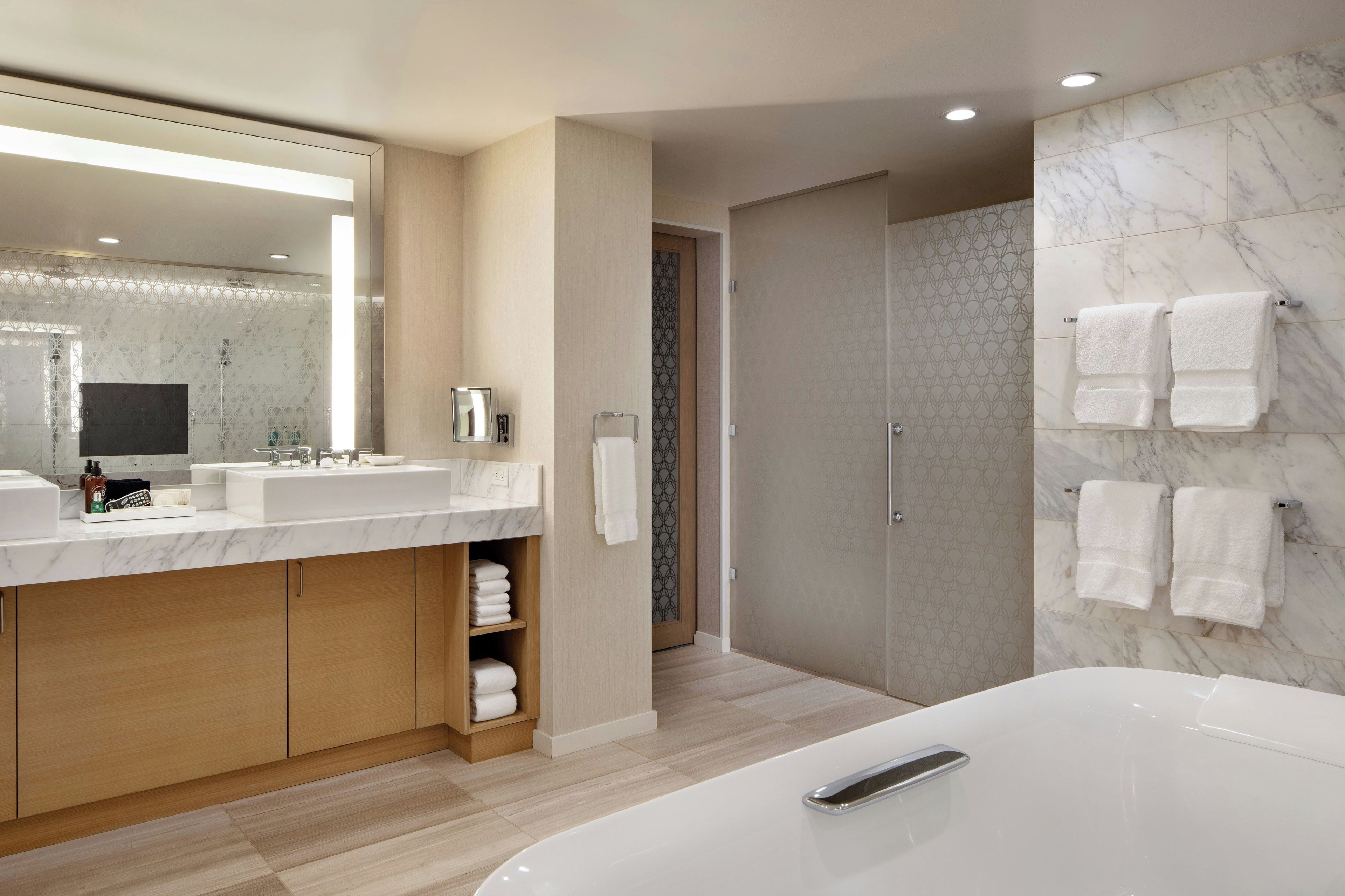 A modern bathroom with a large mirror, two sinks, a walk-in shower, and a bathtub.