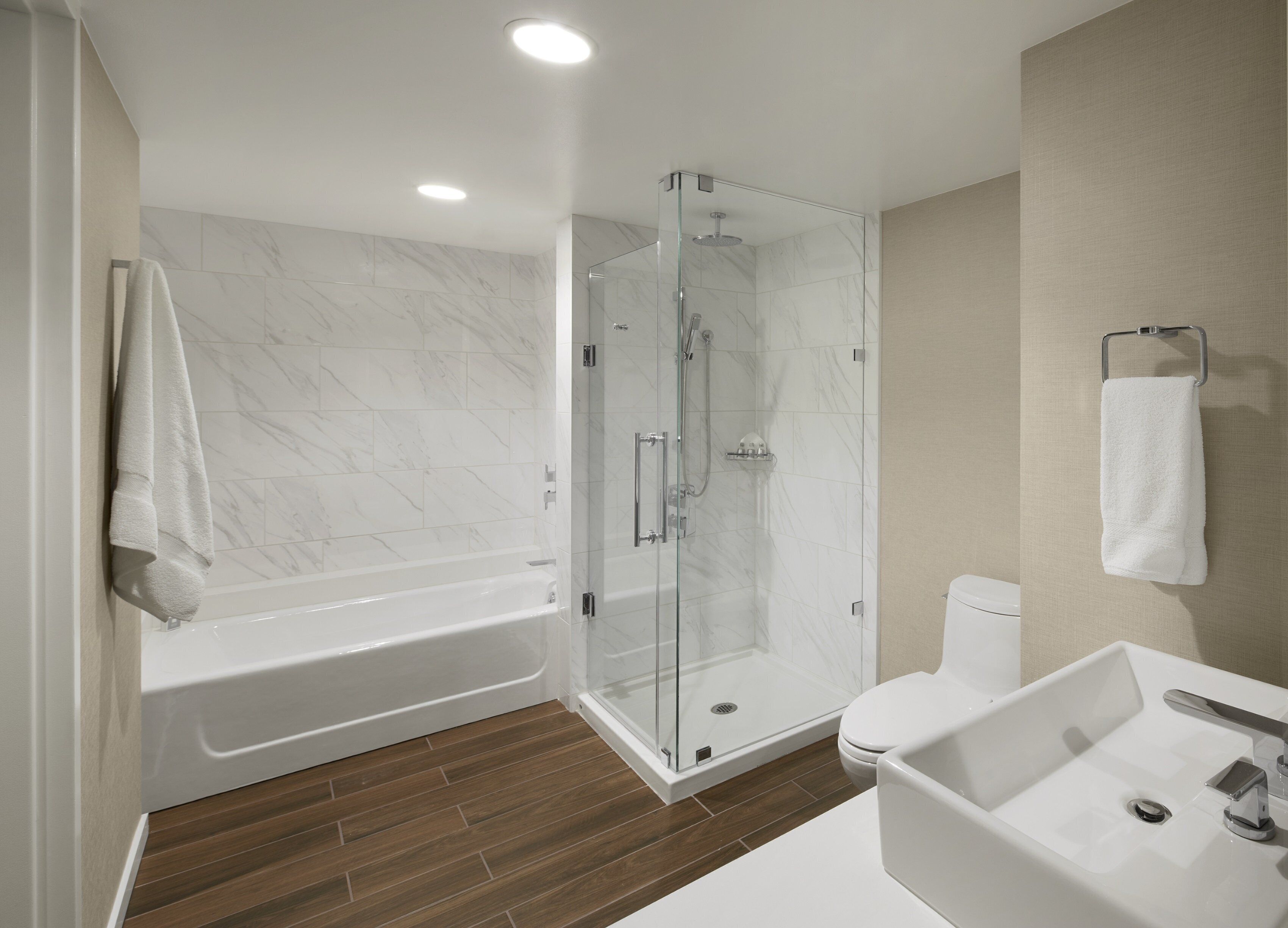 A modern bathroom with a glass-enclosed shower, a white bathtub, and a sink with a mirror.