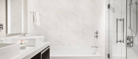 A modern bathroom with a white marble wall, a glass-enclosed shower, and a white bathtub.