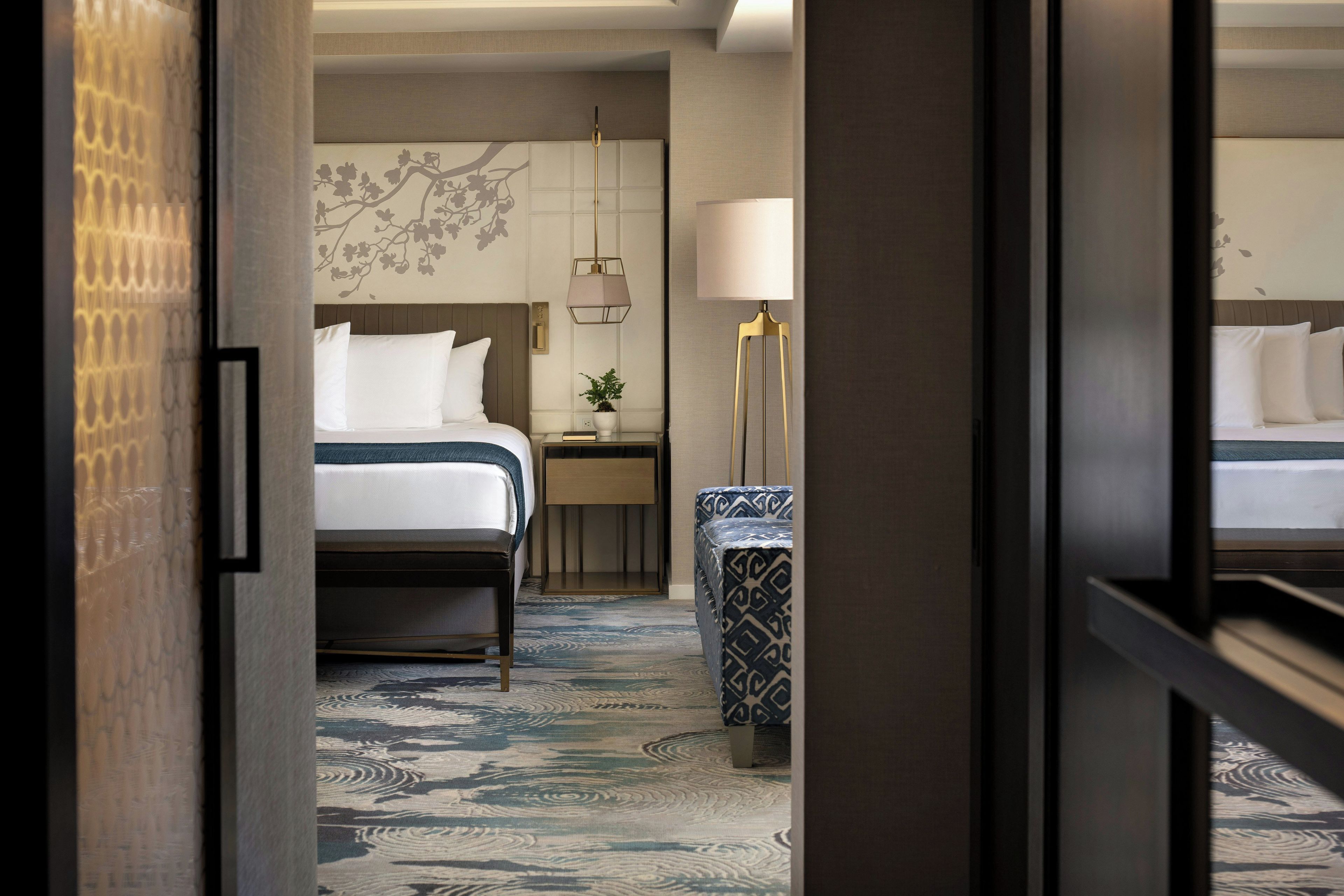 A hotel room with a bed, bedside table, lamp, and patterned carpet.