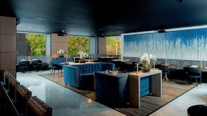 A modern restaurant with a central bar area, seating arrangements, and large windows offering a view of greenery. - Hotel Nikko San Francisco (San Francisco)
