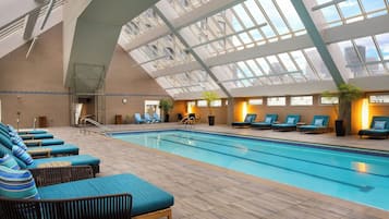 Una piscina interior con sillas de descanso y techo de cristal.