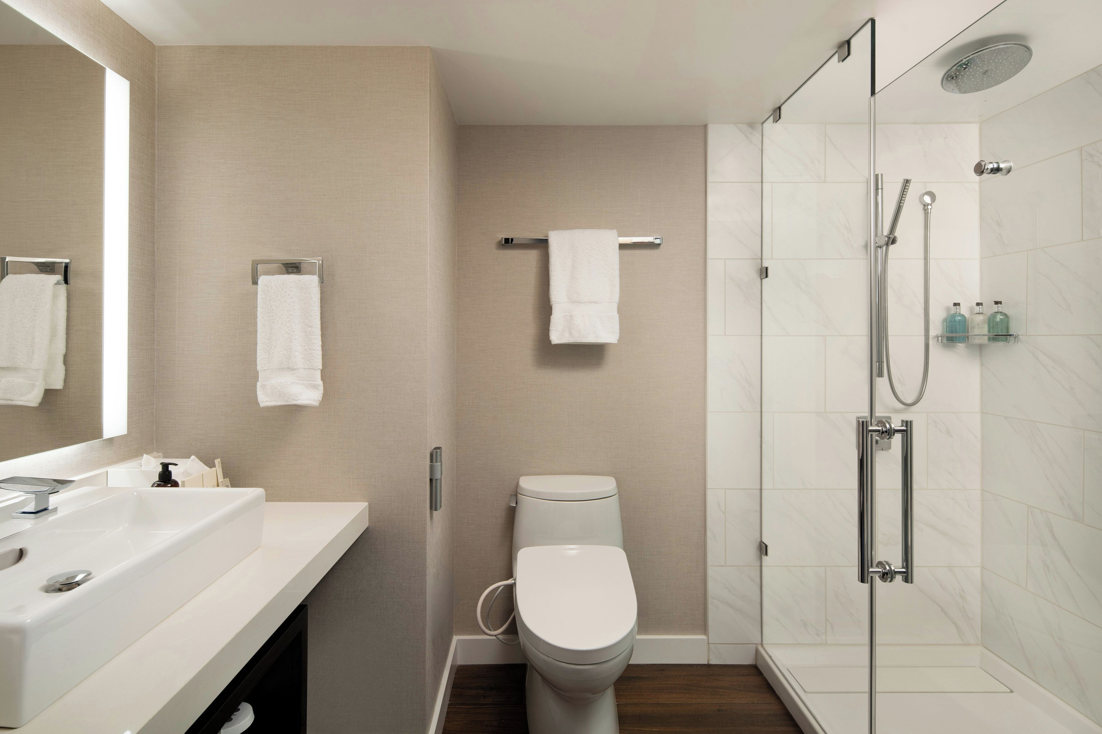 A modern bathroom with a white toilet, a glass-enclosed shower, and a vanity with a mirror.