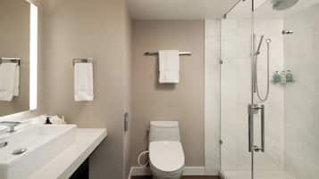 Un baño moderno con inodoro blanco, ducha con mampara de vidrio y tocador con espejo.