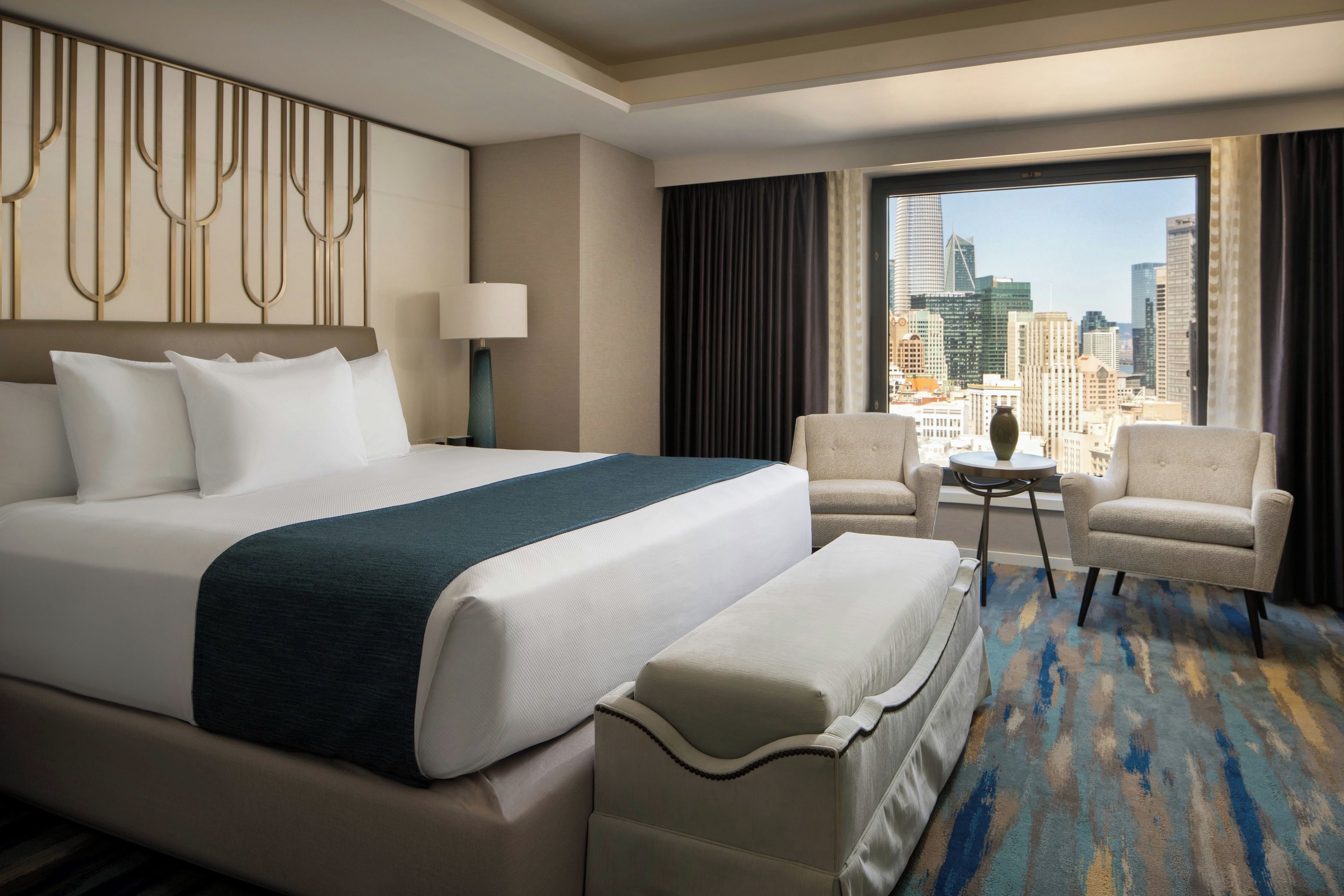 Habitación de hotel con una cama grande, un escritorio, dos sillones y vistas a la ciudad.