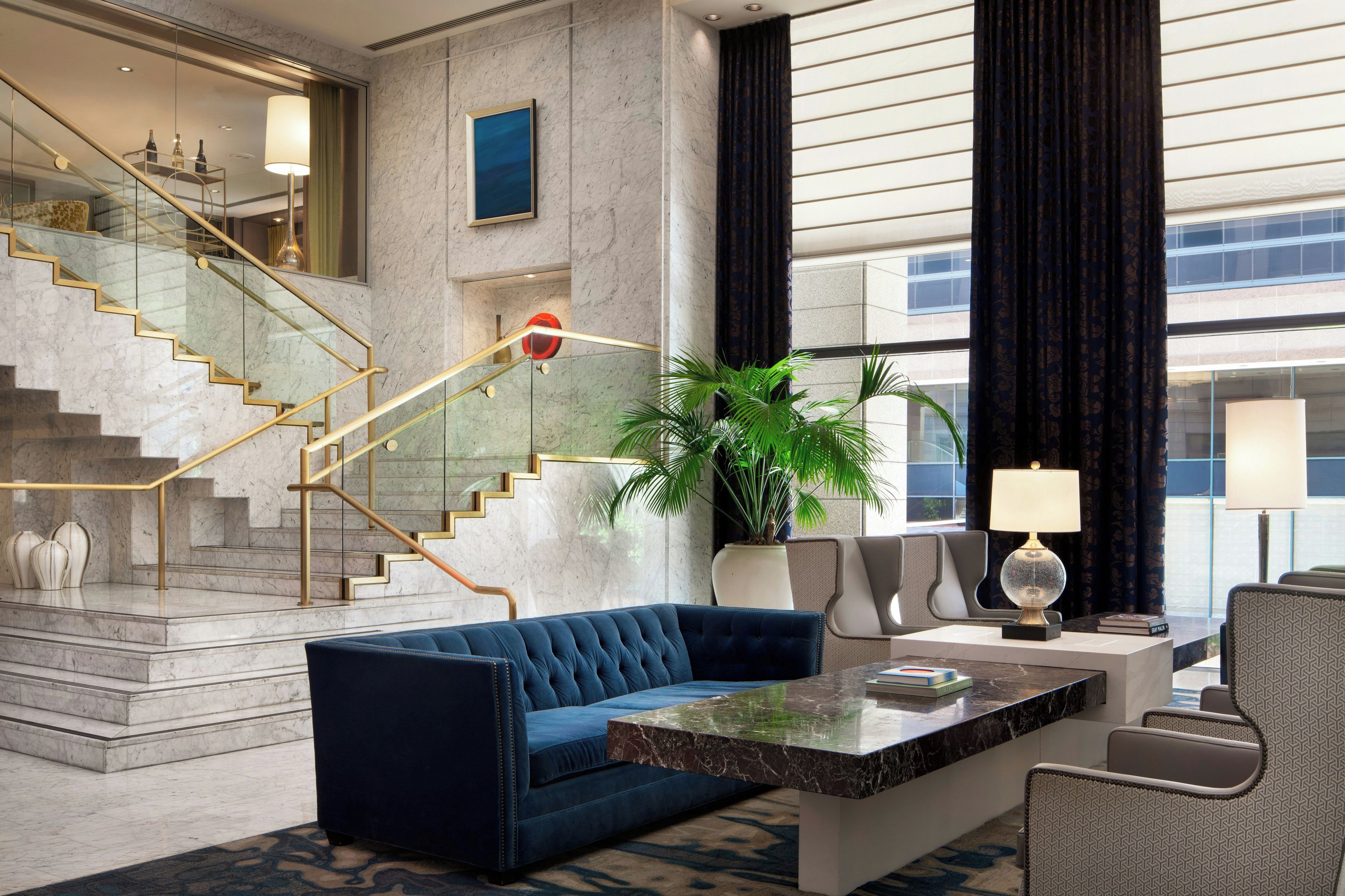 A modern lobby with marble stairs, a blue sofa, a potted plant, and a glass railing.