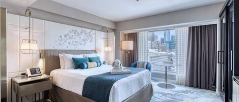 A modern hotel room with a large bed, a desk with a phone, a chair, a small table, and a city view.