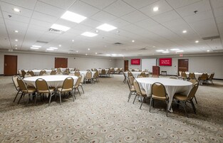 Un salón de conferencias amplio con varias mesas y sillas, piso alfombrado e iluminación en el techo.