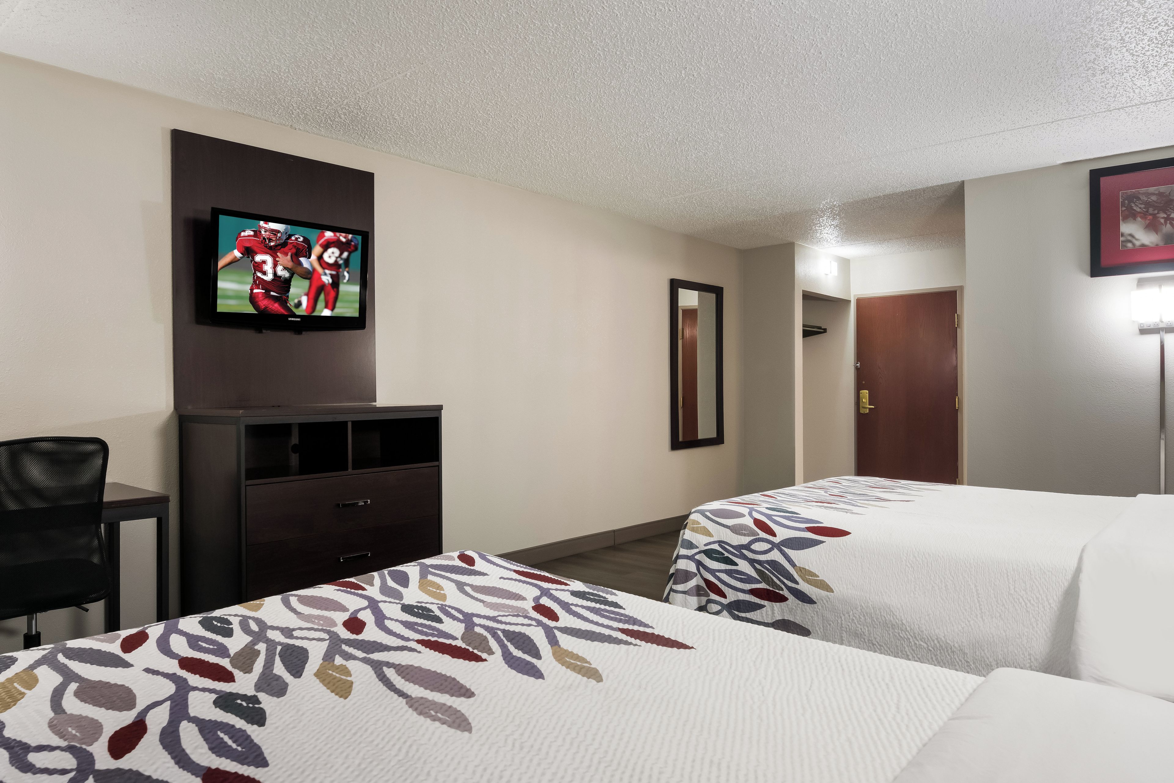 Una habitación de hotel con dos camas, un televisor en la pared, un escritorio y una silla.