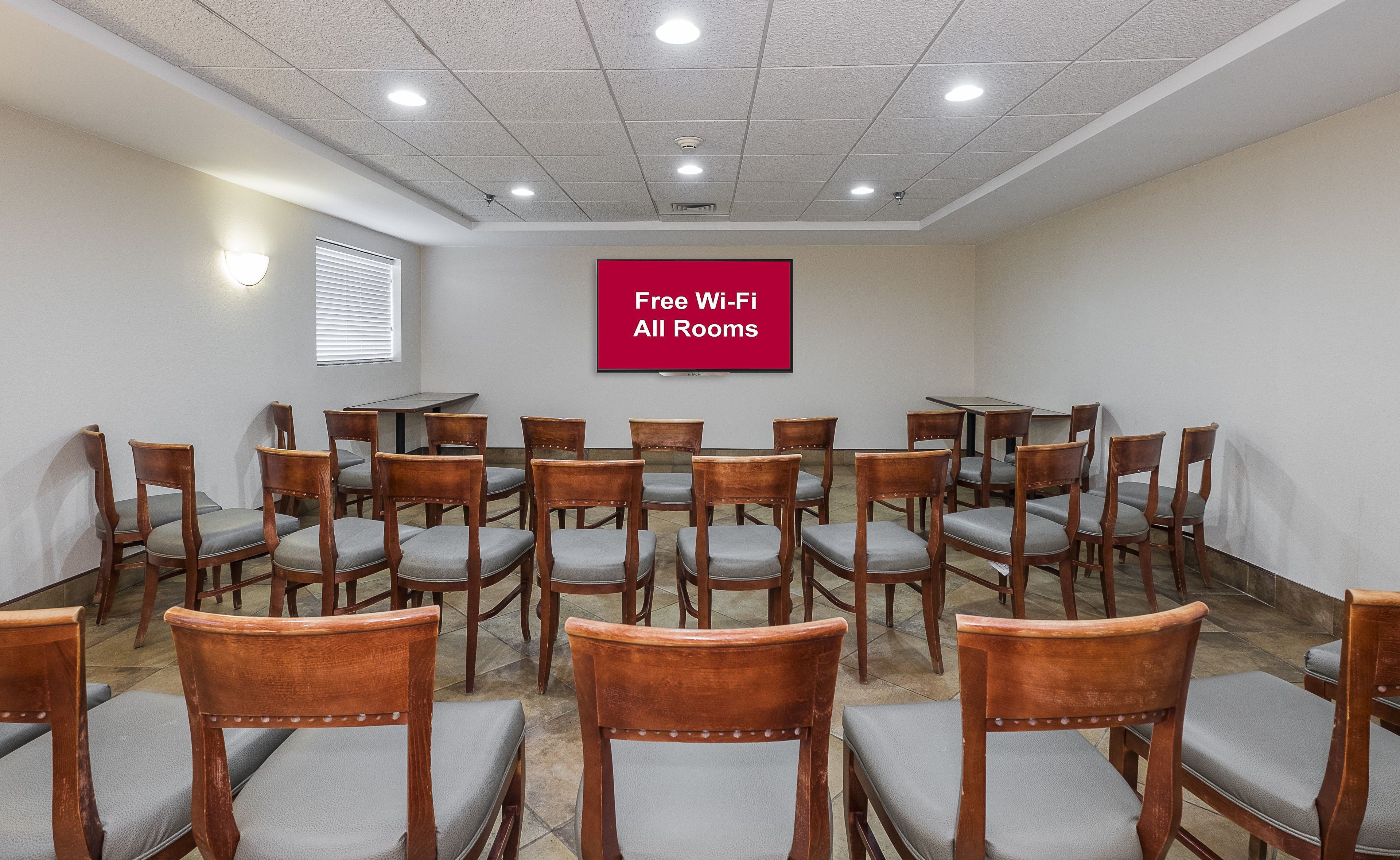 Un salón de conferencias con filas de sillas y mesas de madera, un techo con iluminación empotrada y un cartel que indica acceso gratuito a Wi-Fi.