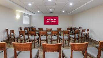 Un salón de conferencias con filas de sillas y mesas de madera, un techo con iluminación empotrada y un cartel que indica acceso gratuito a Wi-Fi.