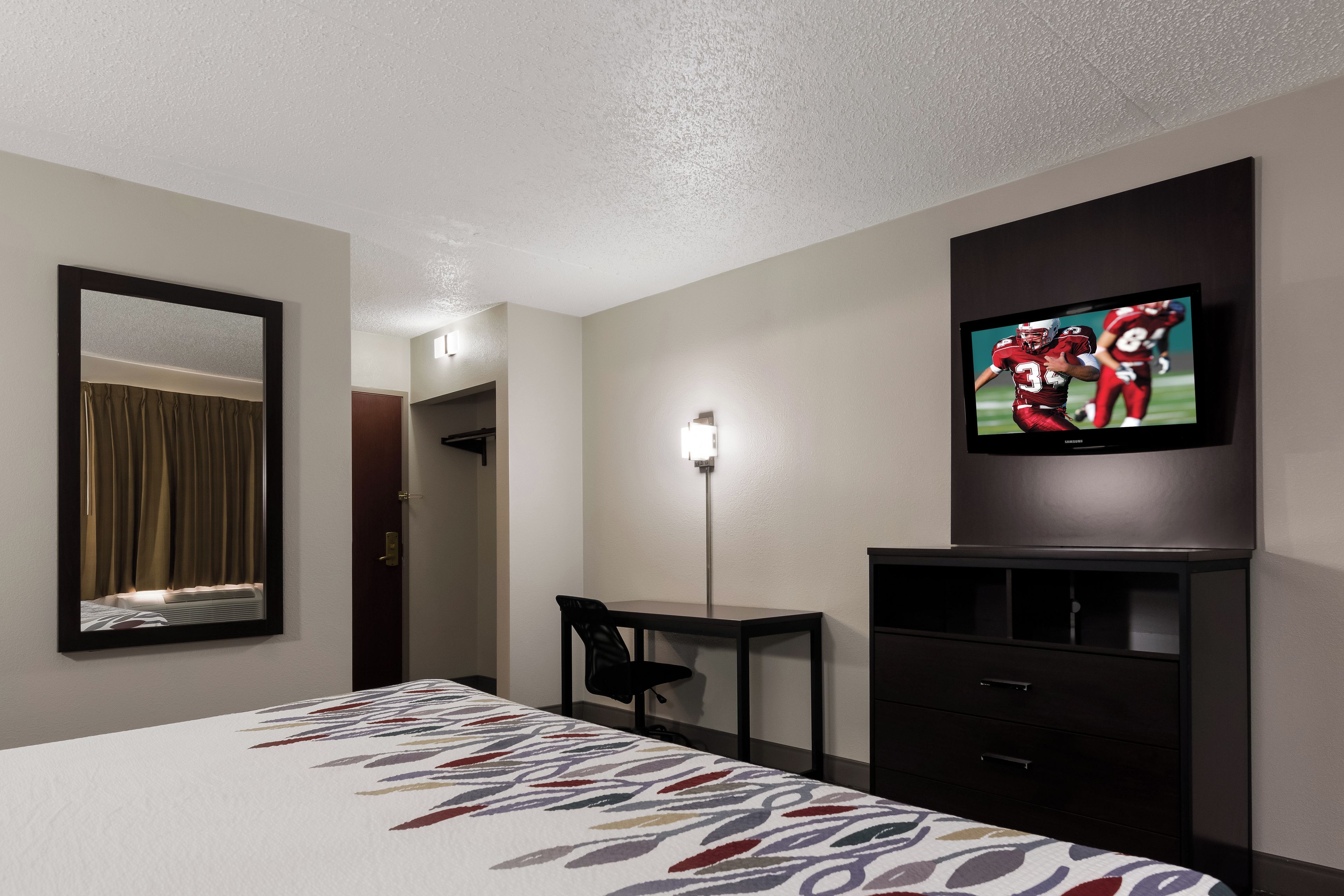 A hotel room with a bed, a desk, a chair, a television, and a mirror.