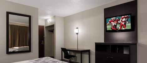 Habitación de hotel con cama, escritorio, silla, televisor y espejo.